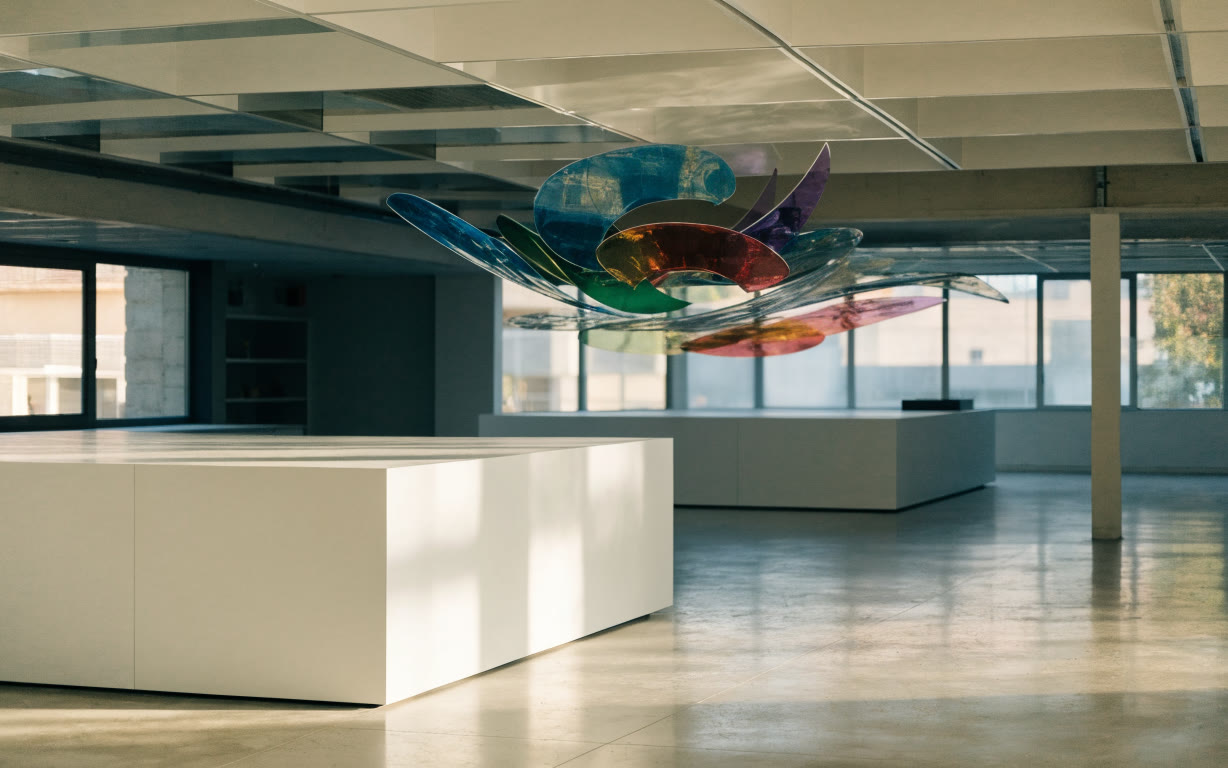 Sala de museo con bases blancas y una instalación de vidrio de colores suspendida