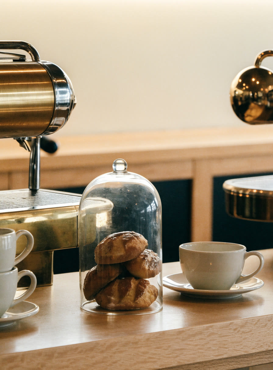 Barra de café con tazas de cerámica y pan dulce bajo campana de vidrio