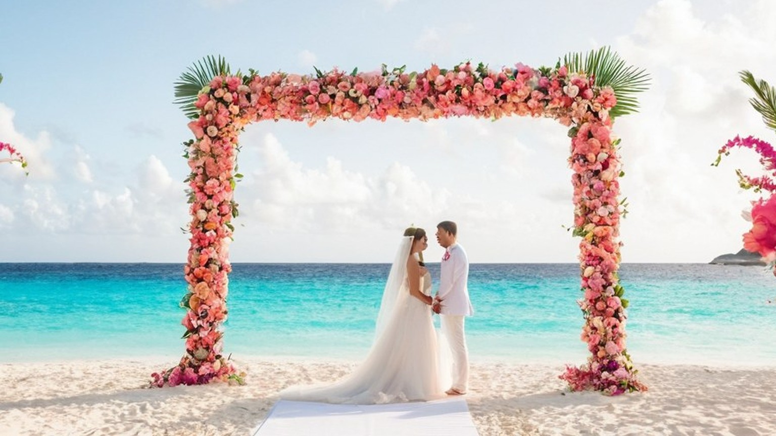 Ceremonia de boda en la playa bajo un arco de flores de coral y fucsia