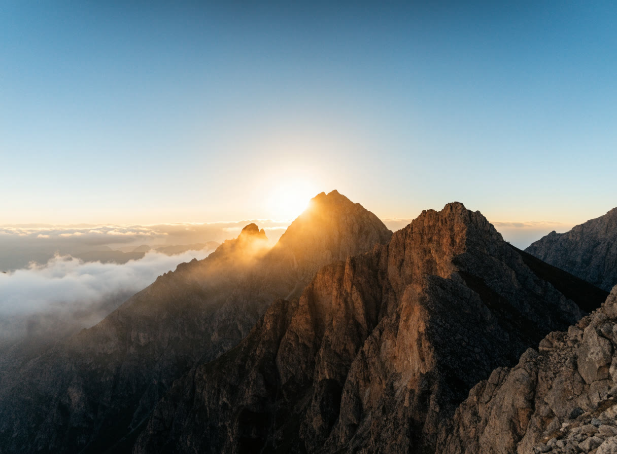 Amanecer dorado detrás de una cumbre rocosa con nubes bajas